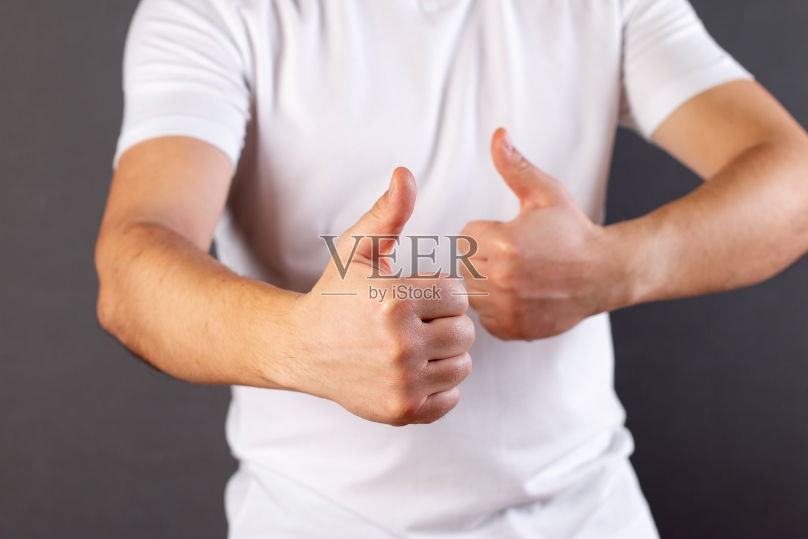 年轻人穿着休闲的白色t恤，露出大拇指向上的手势，胜利者的手势，“班”的手势，一切都好照片摄影图片