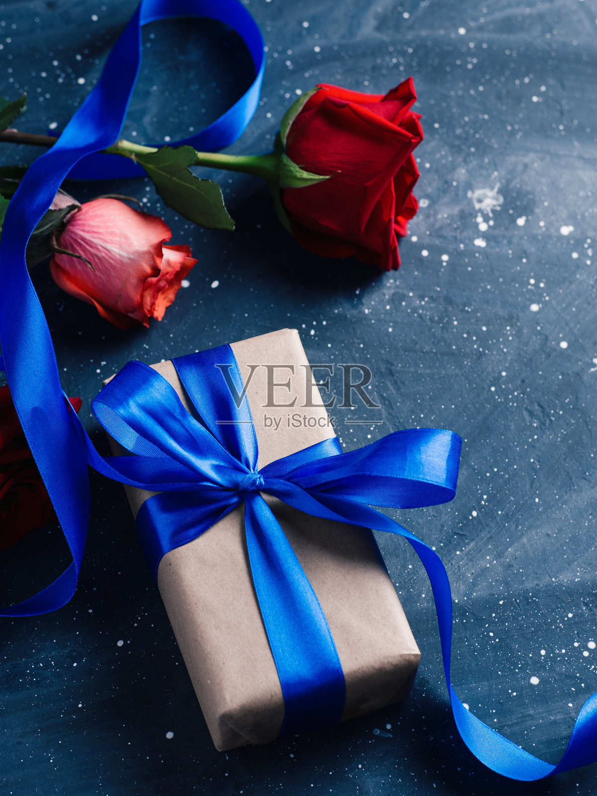一个优雅的礼盒用蓝色的丝带系着，一瓶红酒和一束玫瑰放在黑暗的桌子上，一个浪漫的夜晚。情人节礼物照片摄影图片