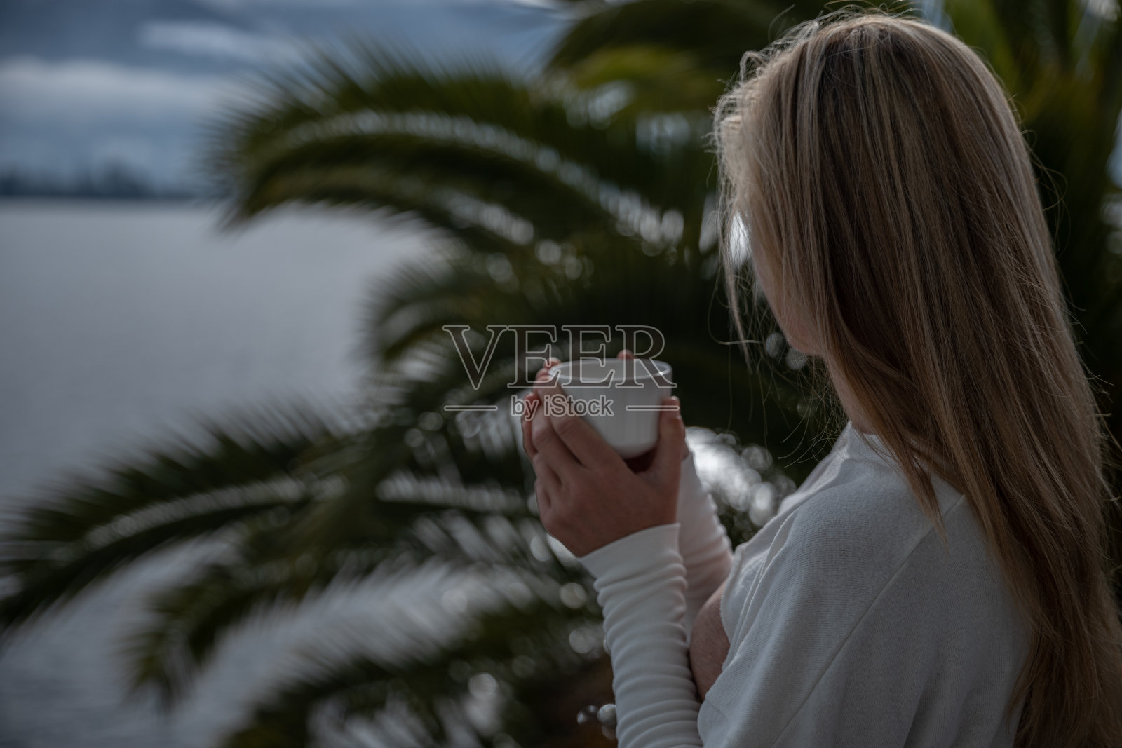 一个年轻女子在她的阳台上喝着茶，可以看到湖景照片摄影图片