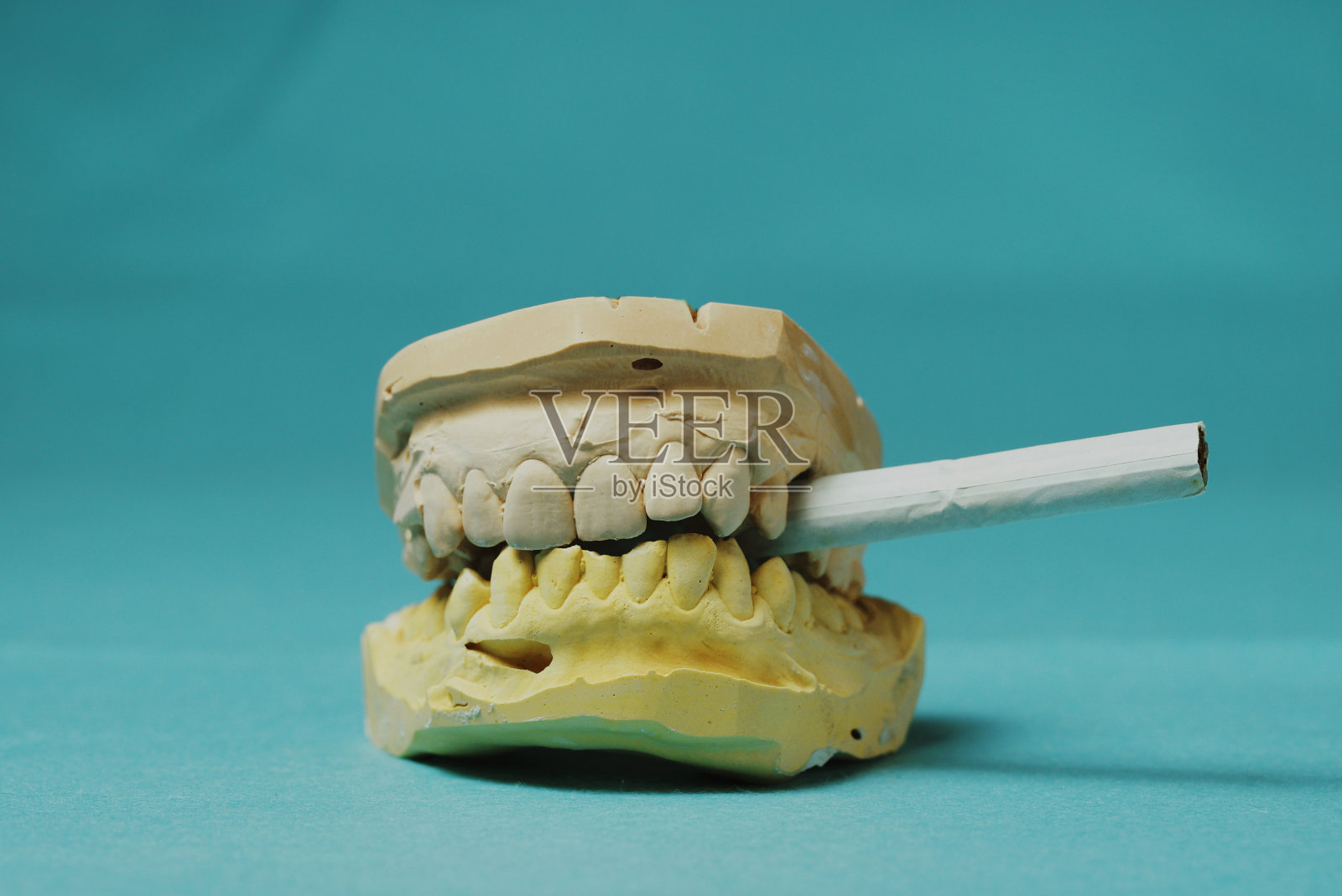 牙齿和香烟的铸造在浅蓝色的背景。烟雾和伤害照片摄影图片