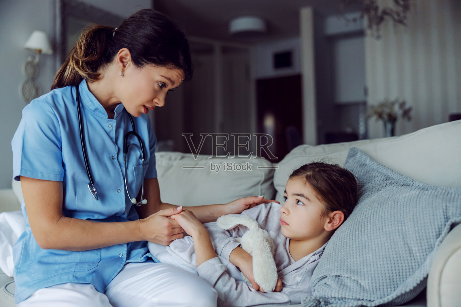 生病的小女孩躺在家里的床上，护士握着她的手。护士在安慰生病的小女孩。照片摄影图片