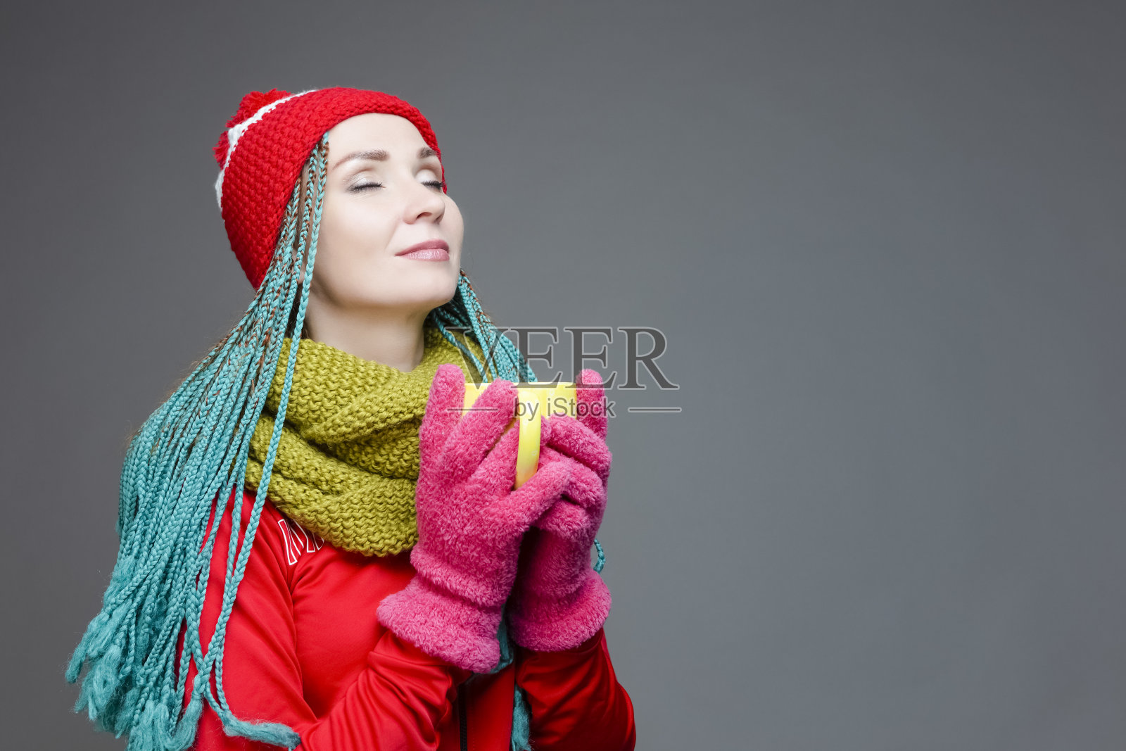 年轻的白人女孩的肖像与绿色的非洲裔美国人的脏辫和暖和的冬天的衣服摆姿势与大茶杯喝。针对灰色。水平的形象照片摄影图片