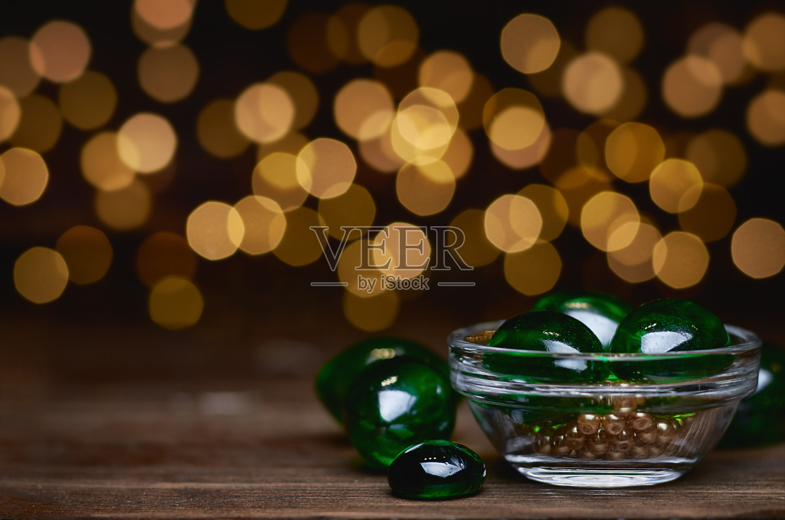 玻璃绿球装在玻璃板上，木制的表面上有黄色的珠子，背景上有黄色模糊的颗粒照片摄影图片