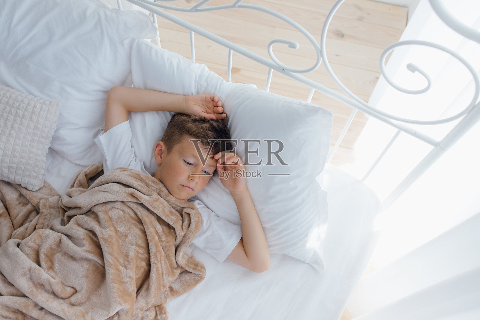 俯视图喜极而泣的可爱的白人小男孩躺在柔软的枕头在舒适的床上照片摄影图片