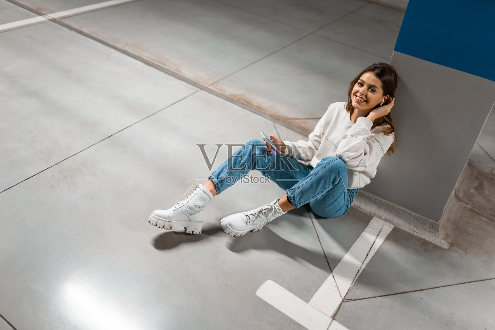 时髦的女孩坐在地下停车场的地板上，用智能手机的无线耳机听音乐照片摄影图片
