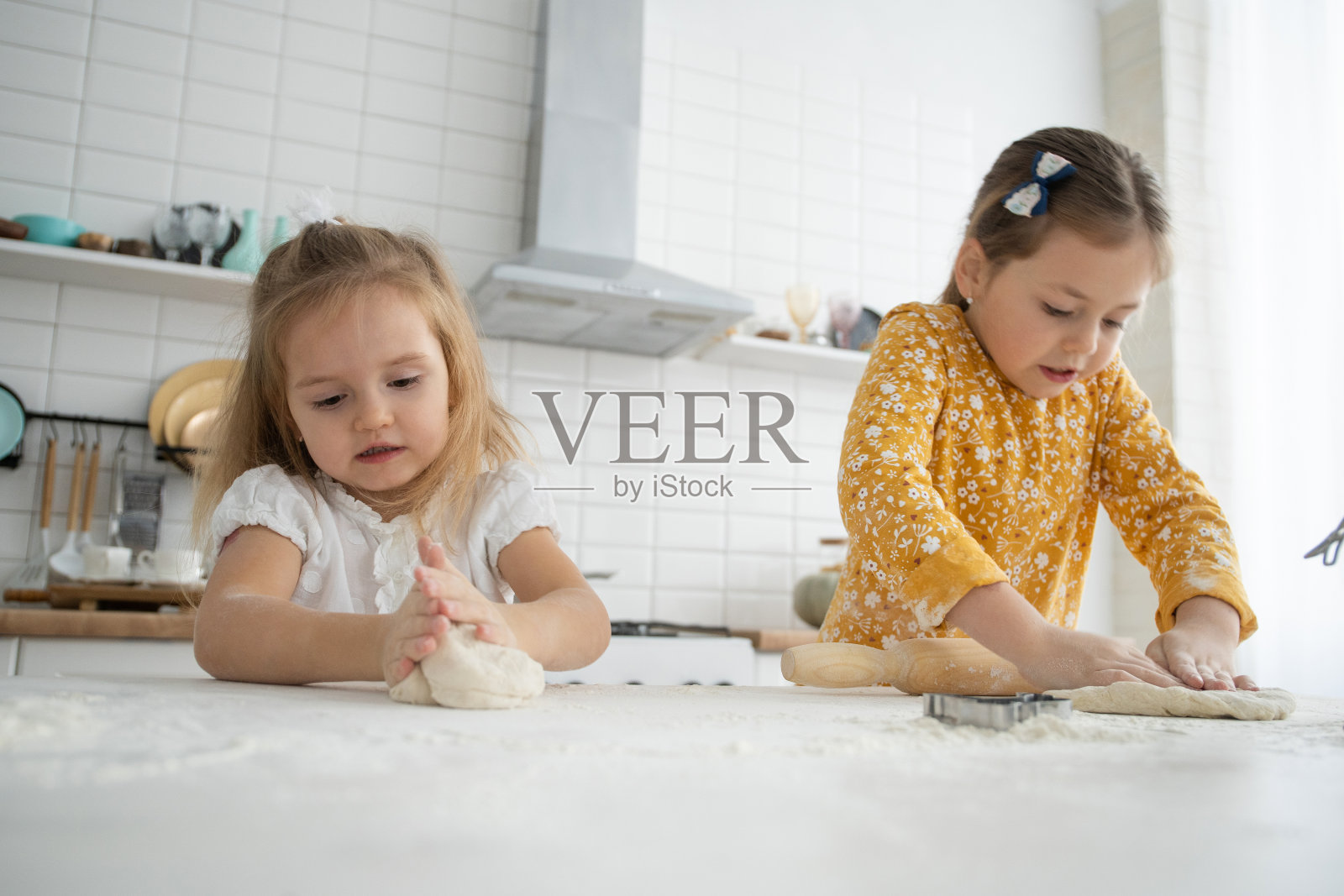 快乐的姐妹儿童女孩烤饼干，揉面团，玩面粉，在厨房大笑。照片摄影图片