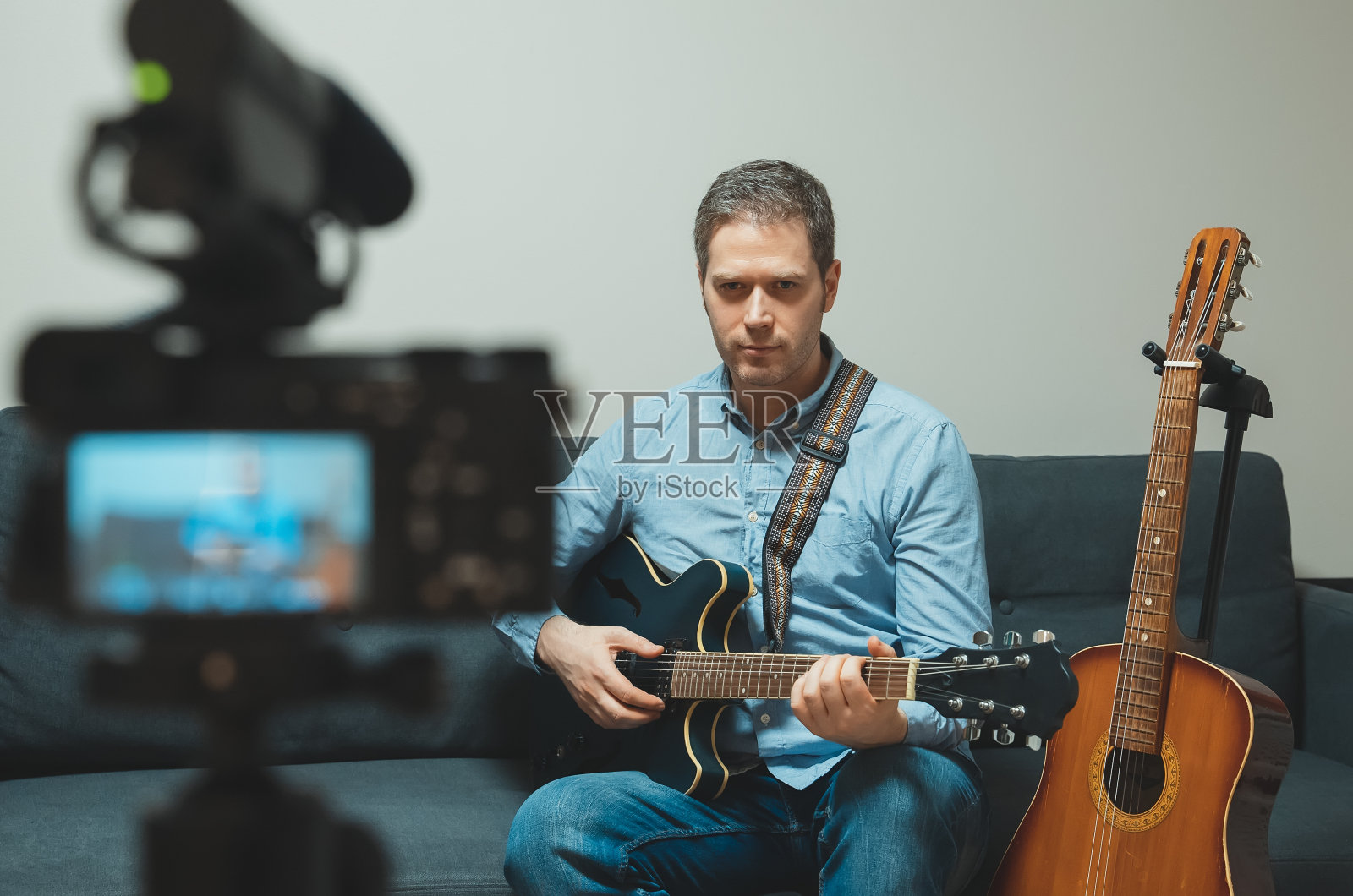 一个拿着半原声吉他的人站在摄像机前。照片摄影图片