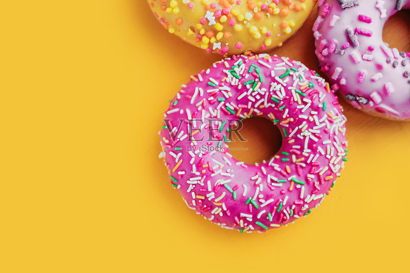 三个圆形的多色粉色和黄色非常开胃的釉面甜甜圈，点缀在明亮的黄色背景上，俯视图，近距离，选择性聚焦照片摄影图片