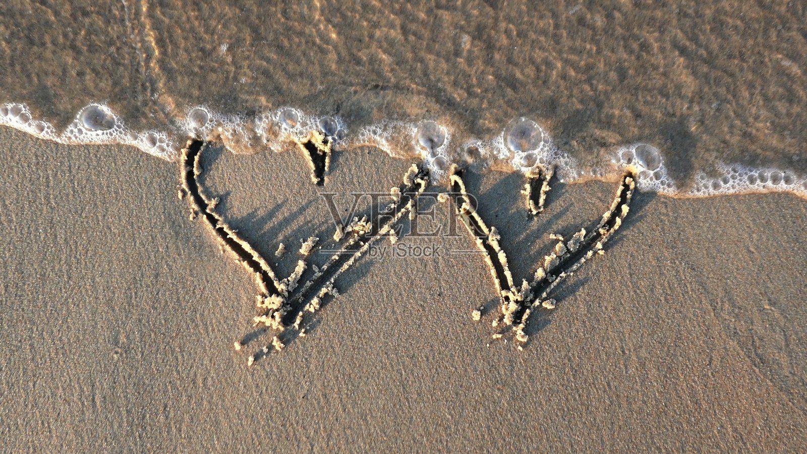 在沙滩上画心形，日落时被海浪抹去照片摄影图片