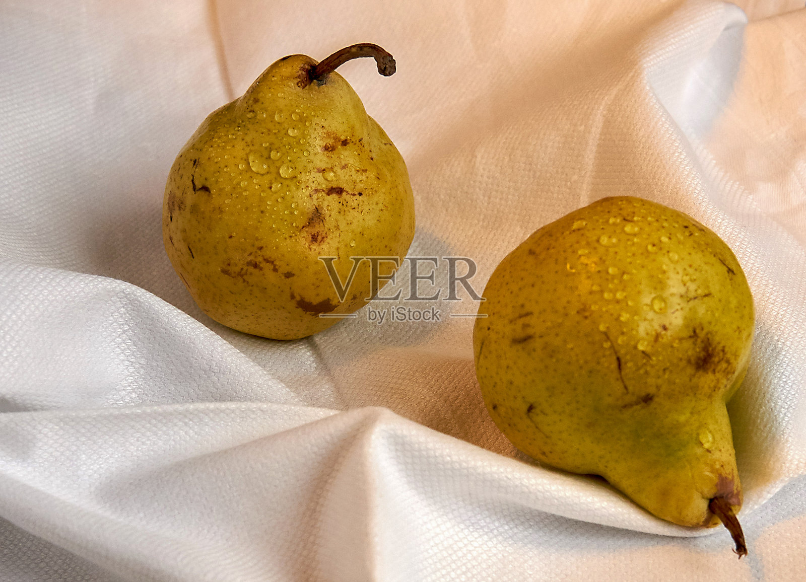 桌上一块白布上放着两个多汁的梨。照片摄影图片