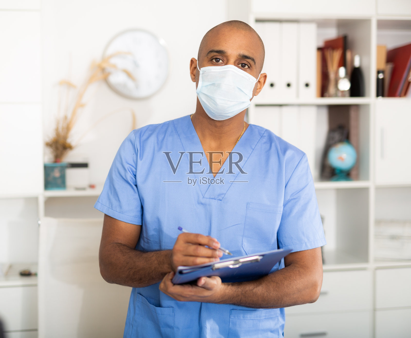 拉丁美洲男护士戴着口罩，在办公室的写字板上写笔记照片摄影图片