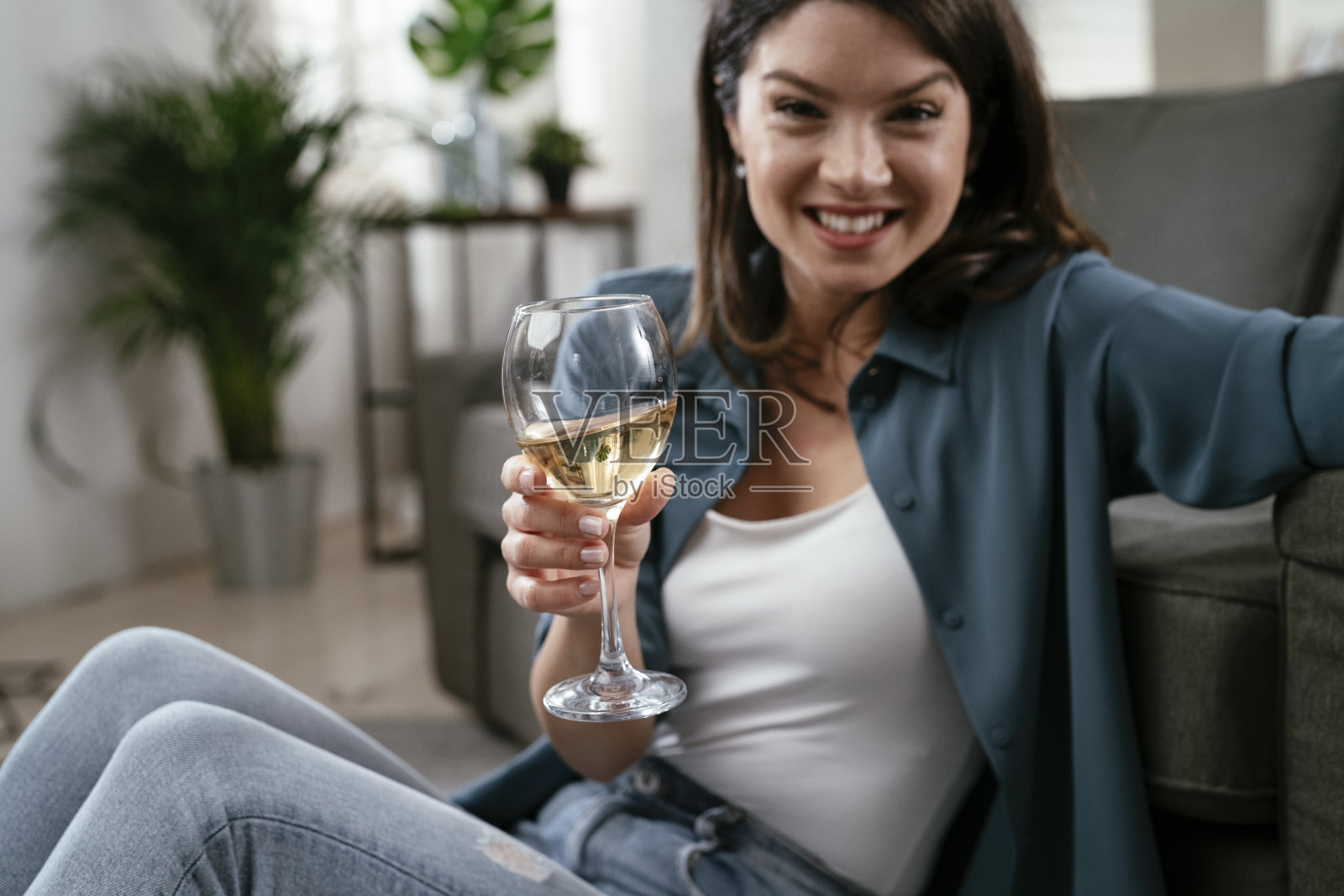 漂亮女人坐在地板上，喝着酒。照片摄影图片