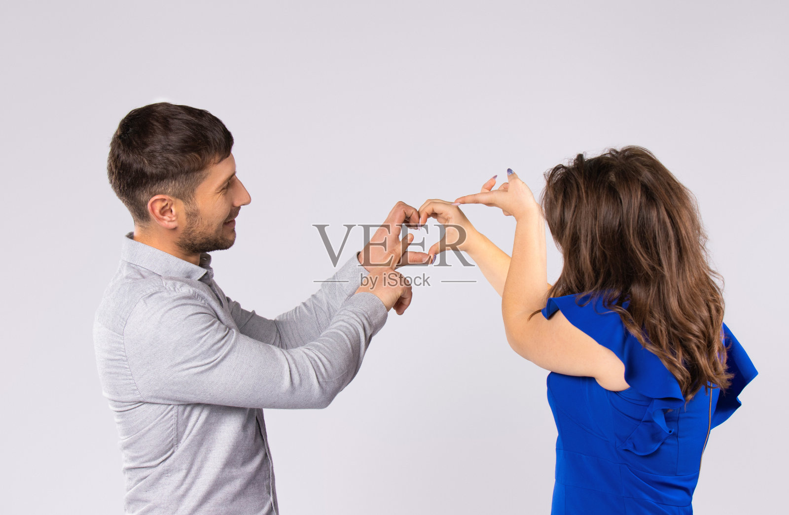 男人和女人用双手做了一个心形，然后用食指指着它。灰色的背景。照片摄影图片