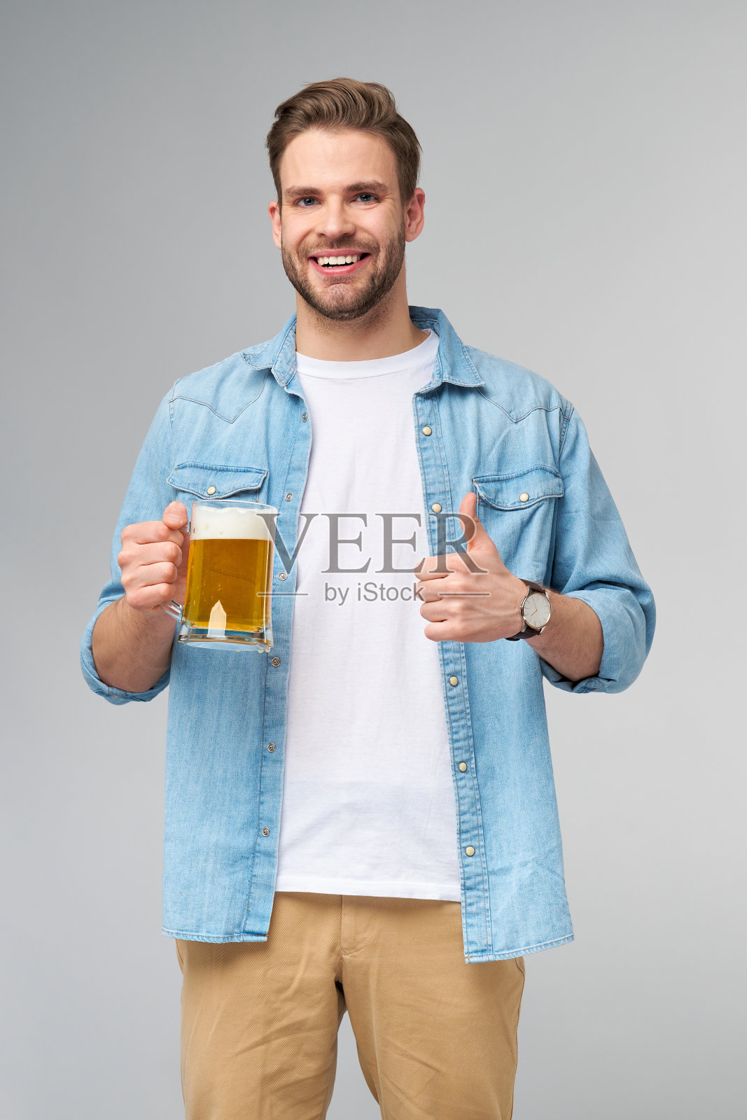 年轻人拿着穿着牛仔裤衬衫拿着一杯啤酒站在灰色背景照片摄影图片