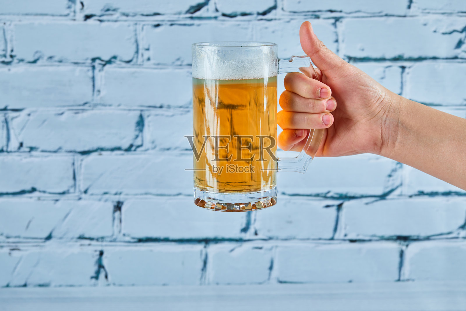 在蓝色背景下拿着一杯啤酒照片摄影图片