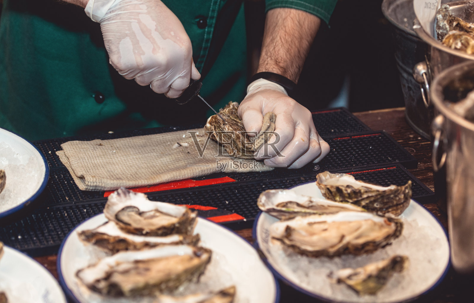 戴白手套的厨师正在用刀剥生蚝。照片摄影图片