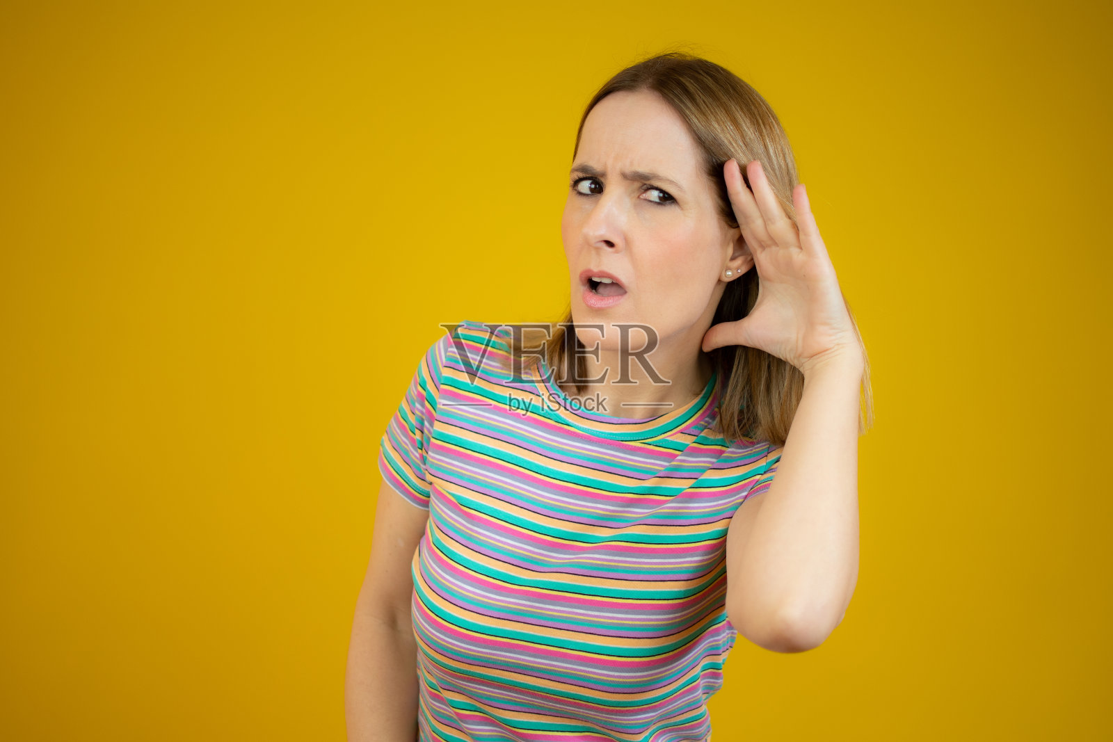 年轻女子在孤立的黄色背景下把手放在耳朵上听着什么照片摄影图片