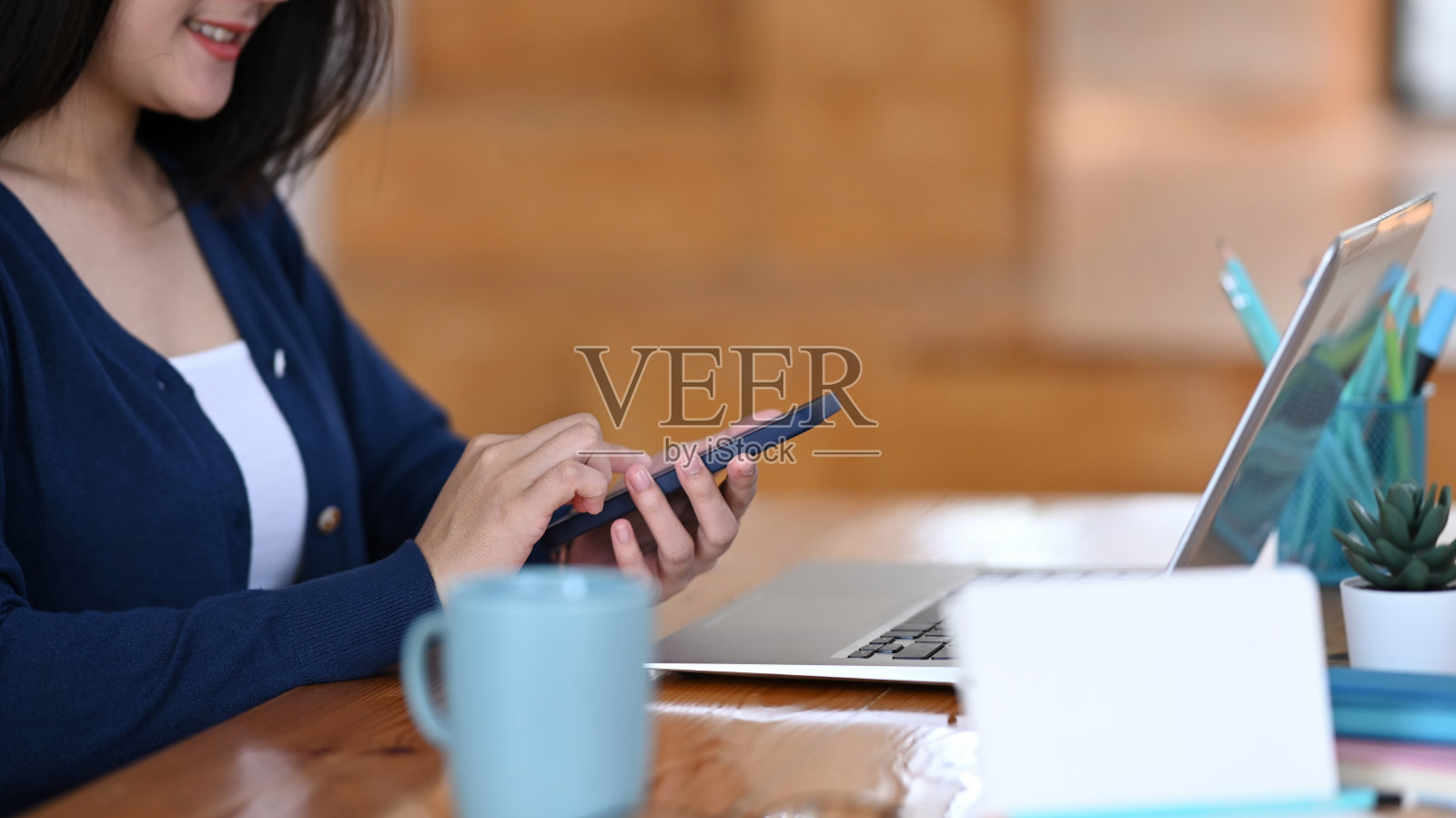 女性拿着智能手机和使用笔记本电脑坐在办公室的裁剪图像。照片摄影图片