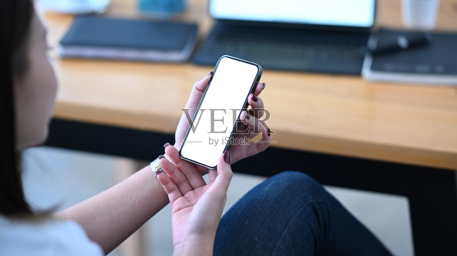 年轻女子坐在她舒适的工作场所，使用手机。白色空白屏幕的广告文本。照片摄影图片