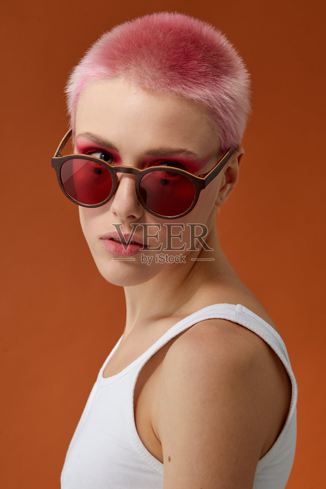 粉红色短发的女孩戴着墨镜，棕色背景。照片摄影图片
