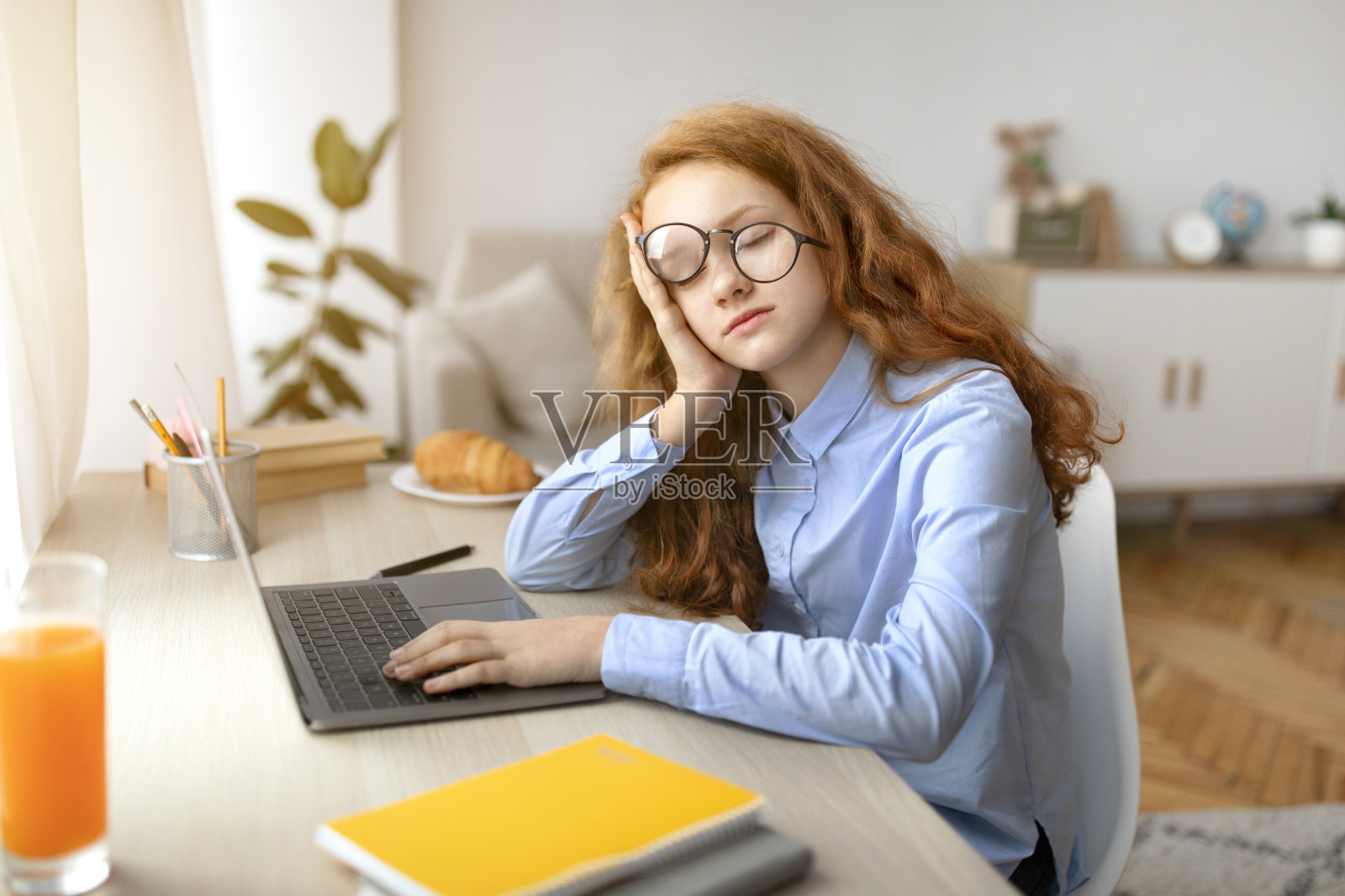 累了的女孩坐在书桌前拿着笔记本电脑睡觉照片摄影图片