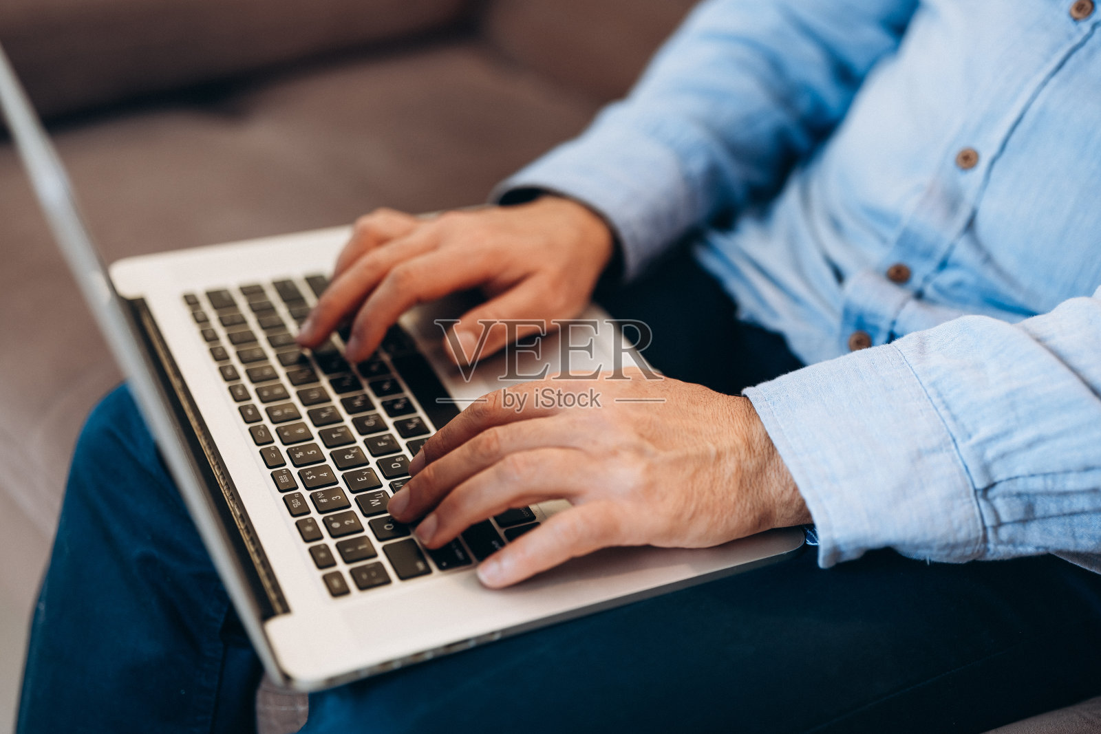 靠近男性在键盘上打字的手。中年男子使用现代笔记本电脑阅读新闻或回复电子邮件。蓝色的衬衫和牛仔裤。现代技术的概念。照片摄影图片