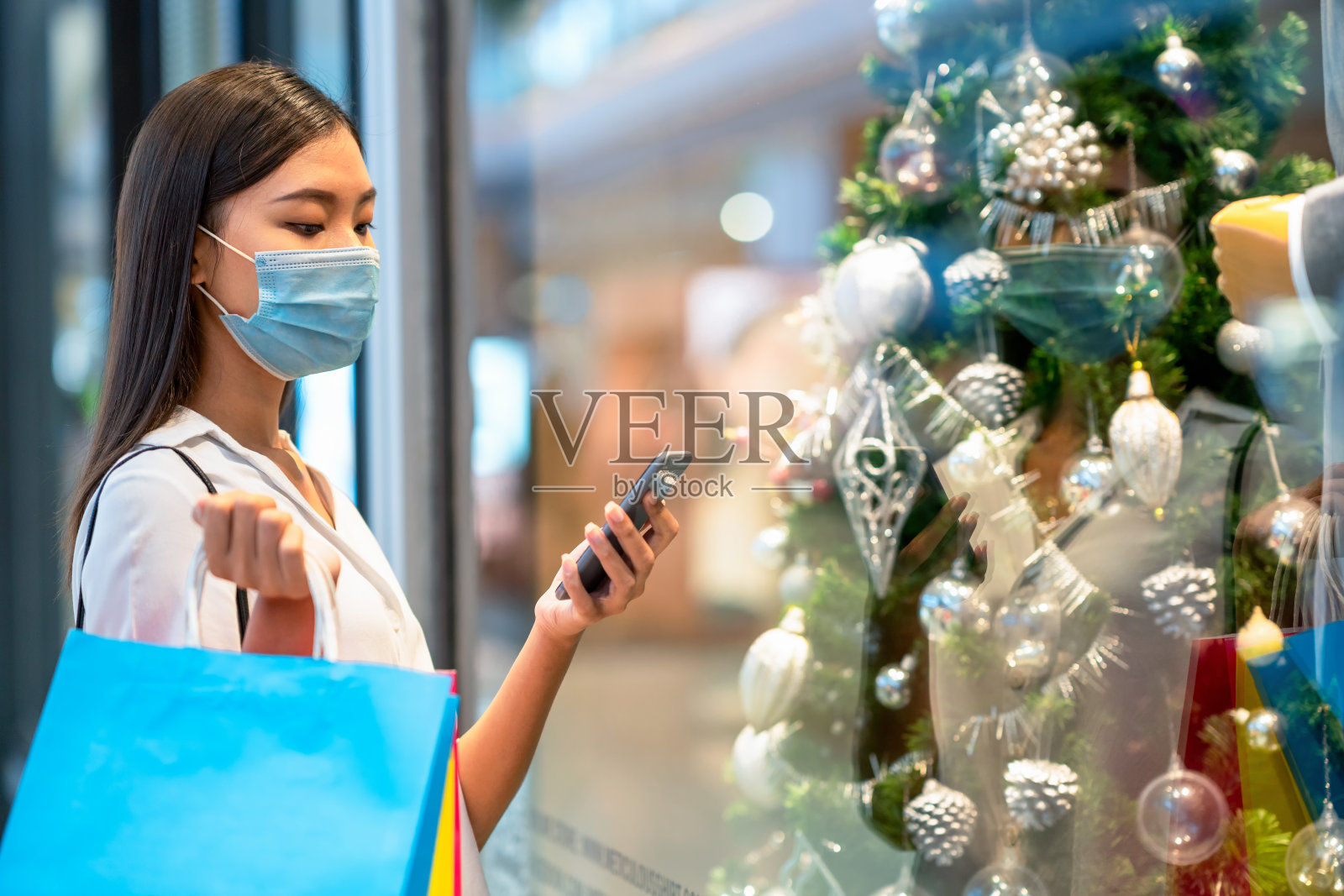 流行期间佩戴防护口罩和购物的时尚女性。她去服装店前用智能手机选购。照片摄影图片