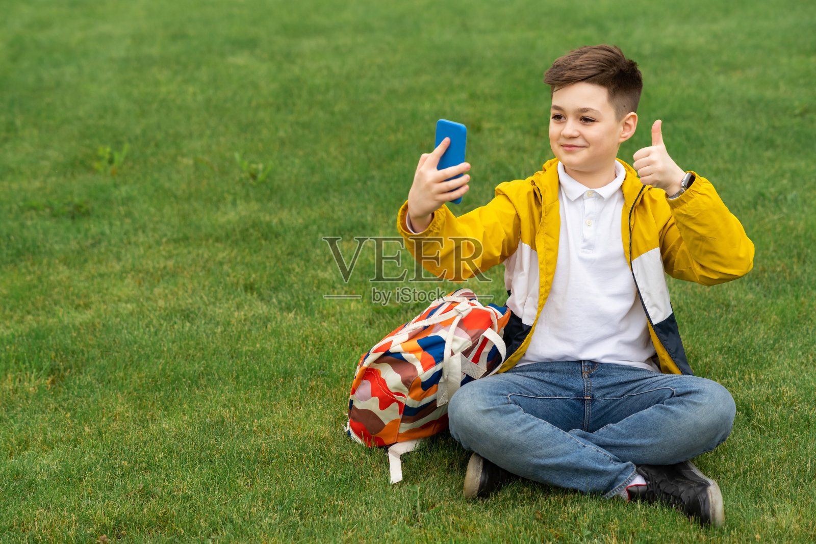 男青少年在草坪上竖起大拇指，在视频通话中交谈照片摄影图片