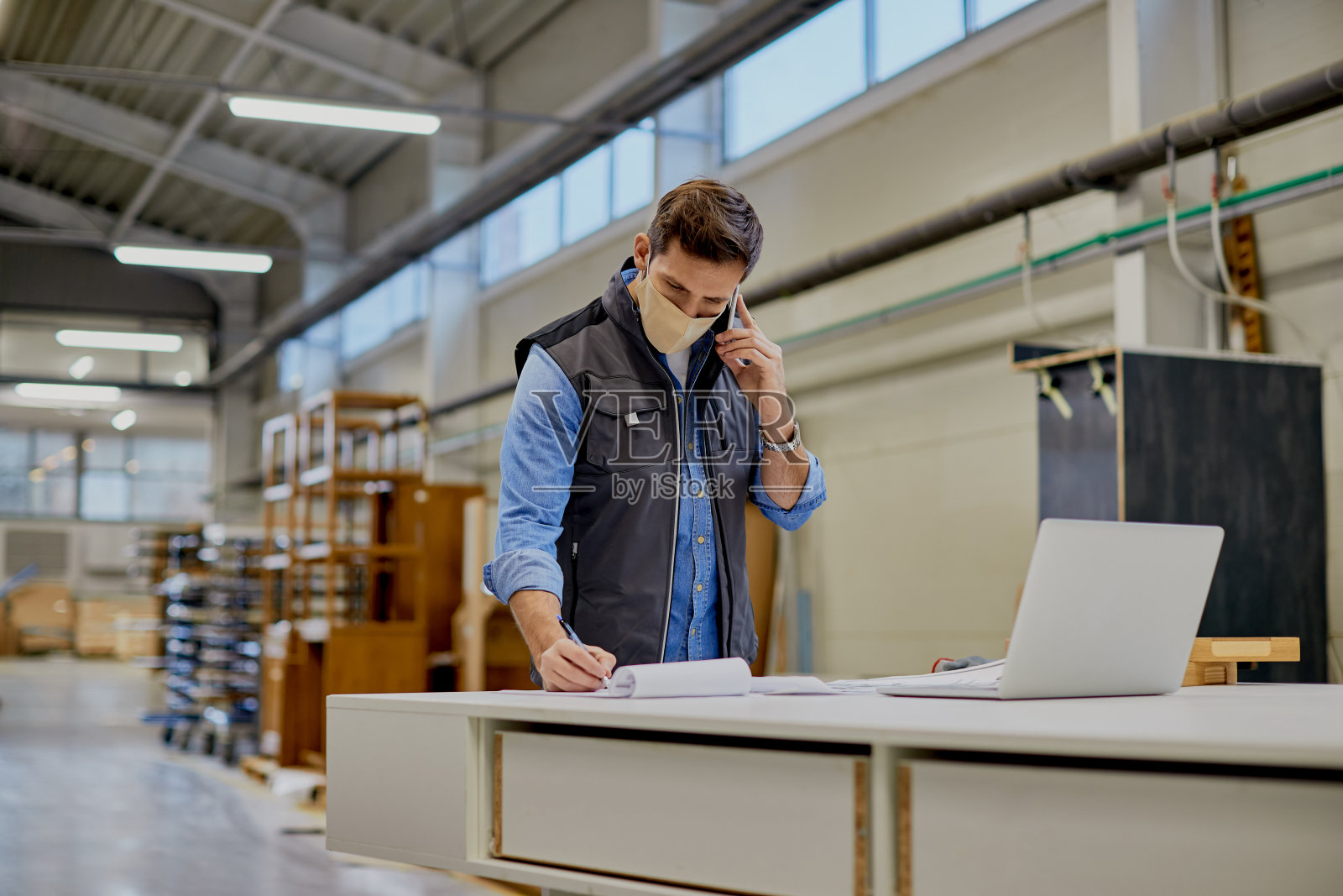 木工工厂的木匠戴着防护口罩打电话和做笔记。照片摄影图片