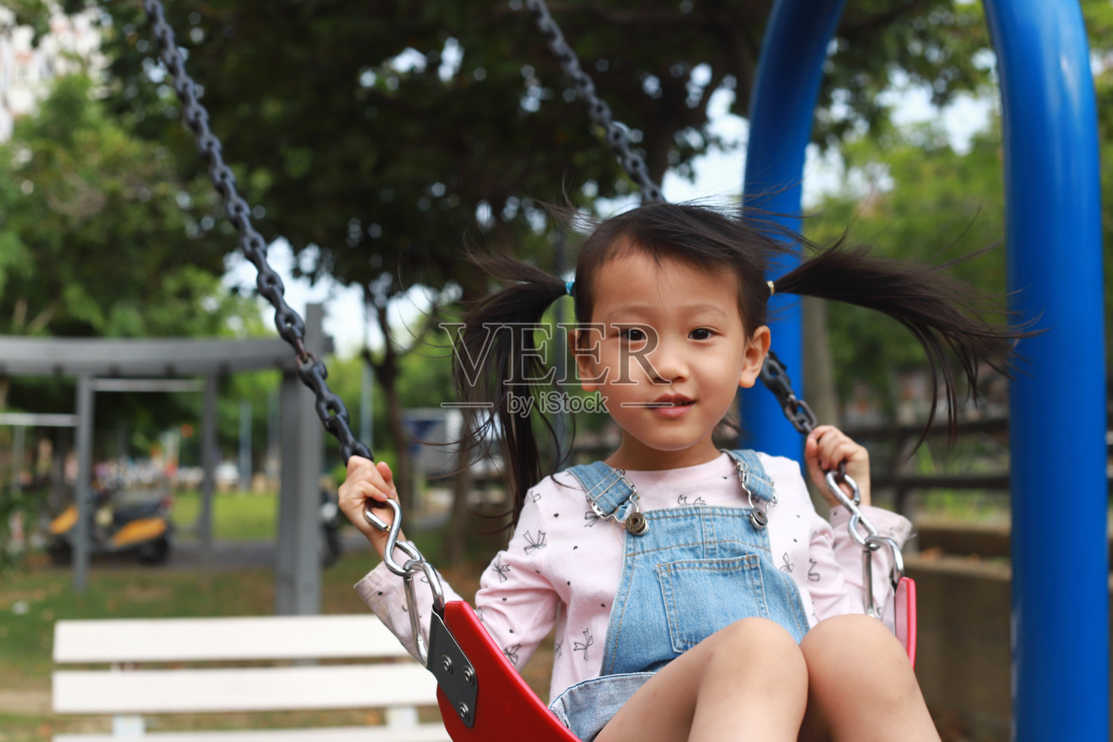 一个微笑的亚洲女孩坐在公园的跷跷板上照片摄影图片
