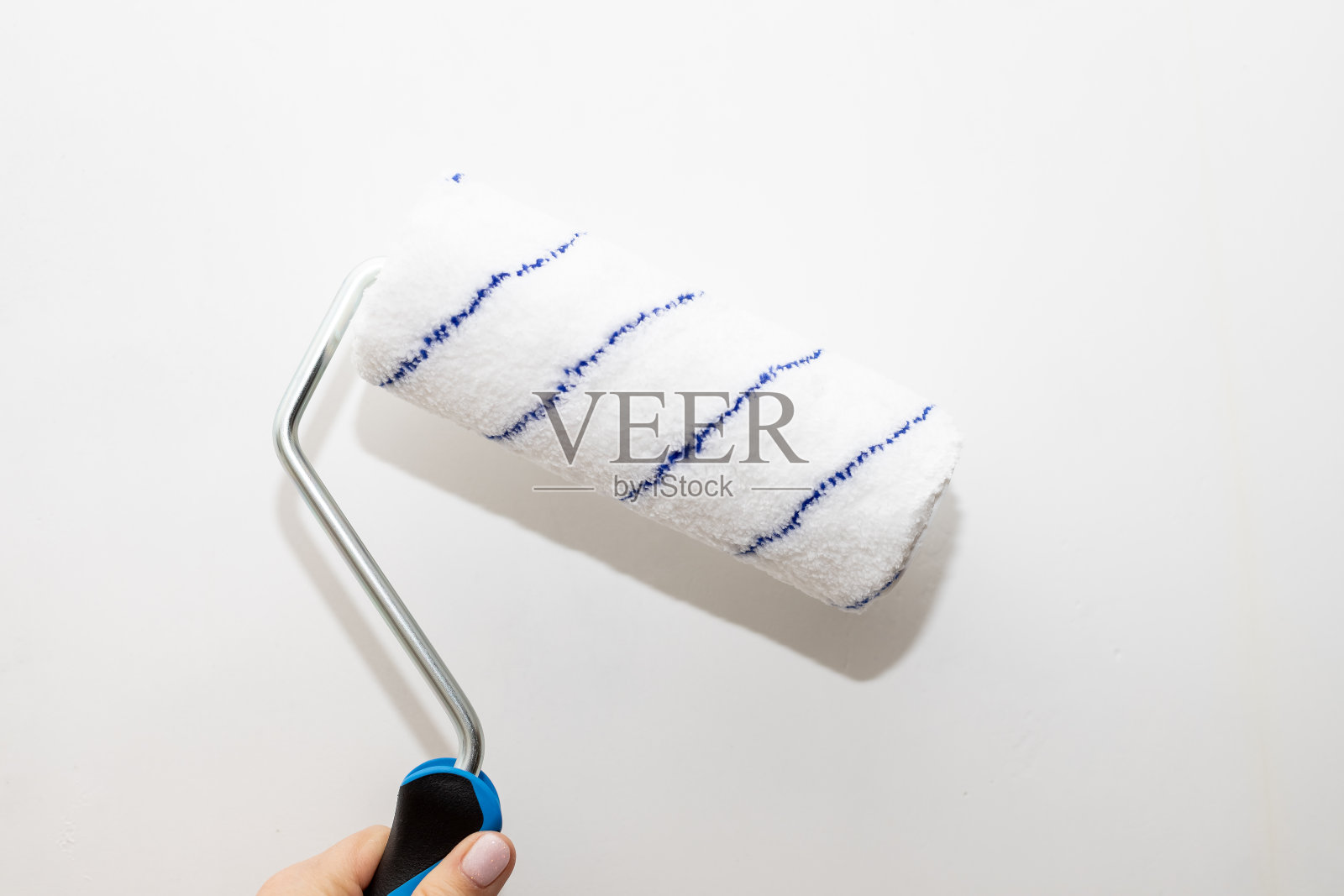 男手拿着一个滚轴，用来刷墙。油漆工把装饰性的油漆涂在墙上。屋内修理。辊壁画。工人准备油漆，家庭翻新。家里装修照片摄影图片