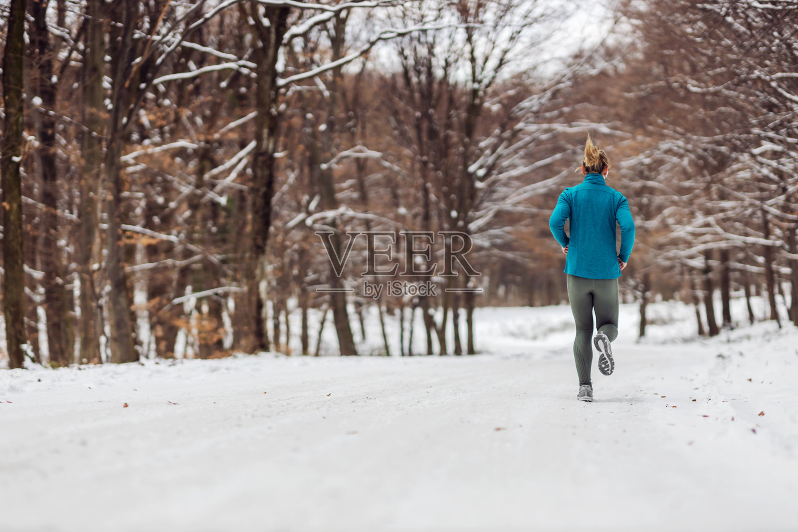 后视图的运动员在一个下雪的天气在自然慢跑。天气冷，下雪，健康生活，健身，健康习惯照片摄影图片