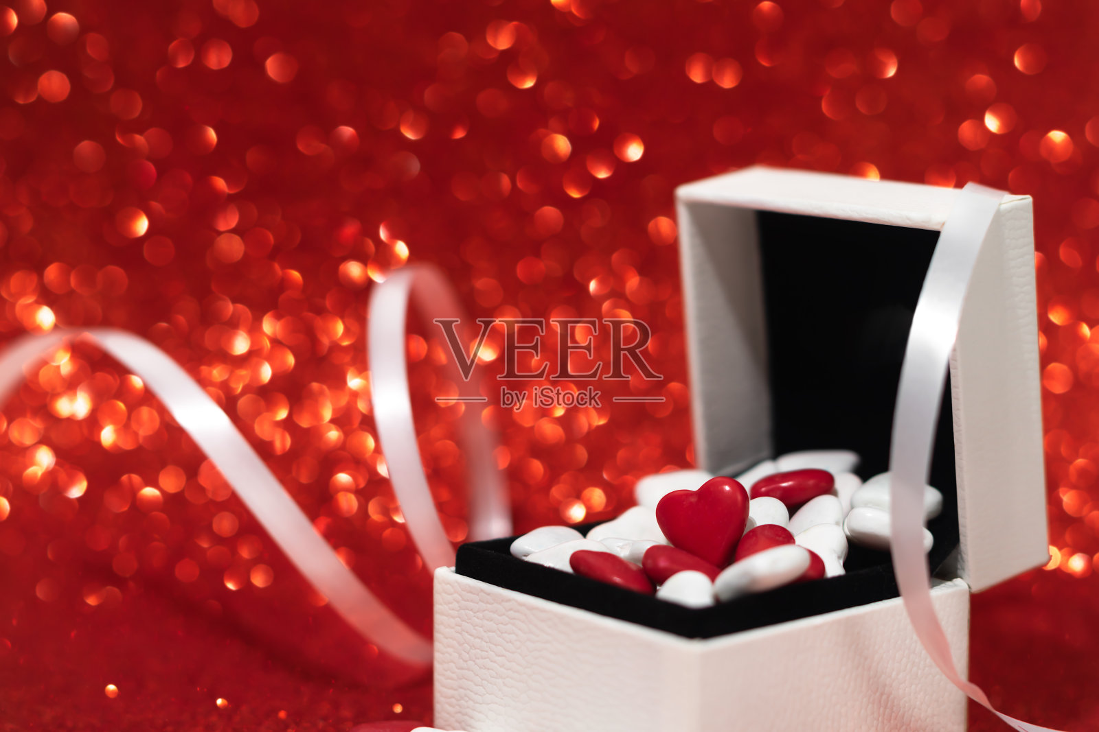 情人节的礼盒里装满了糖果，背景是闪闪发光的红色。照片摄影图片
