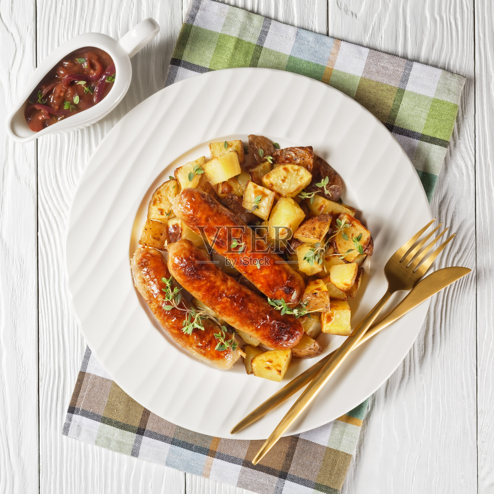 白色木桌上的罐子里盛着洋葱汁，白盘子上放着香肠和烤土豆照片摄影图片