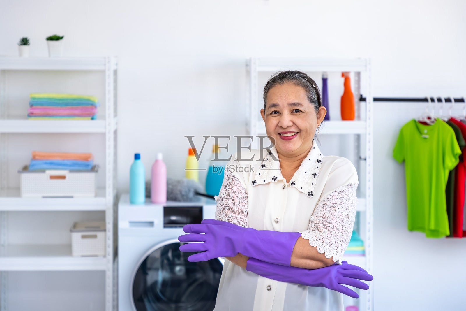 亚洲老年妇女戴着橡胶手套和交叉手臂在洗衣房带着骄傲，看着相机，春季大扫除的概念照片摄影图片