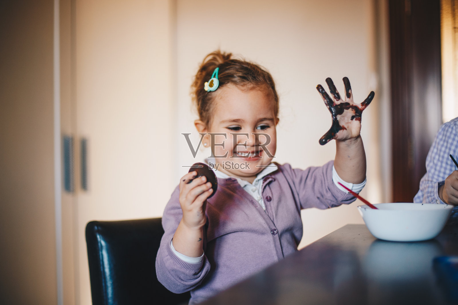 小女孩微笑着，她拿着画好的鸡蛋。她的双手沾满了水彩。照片摄影图片