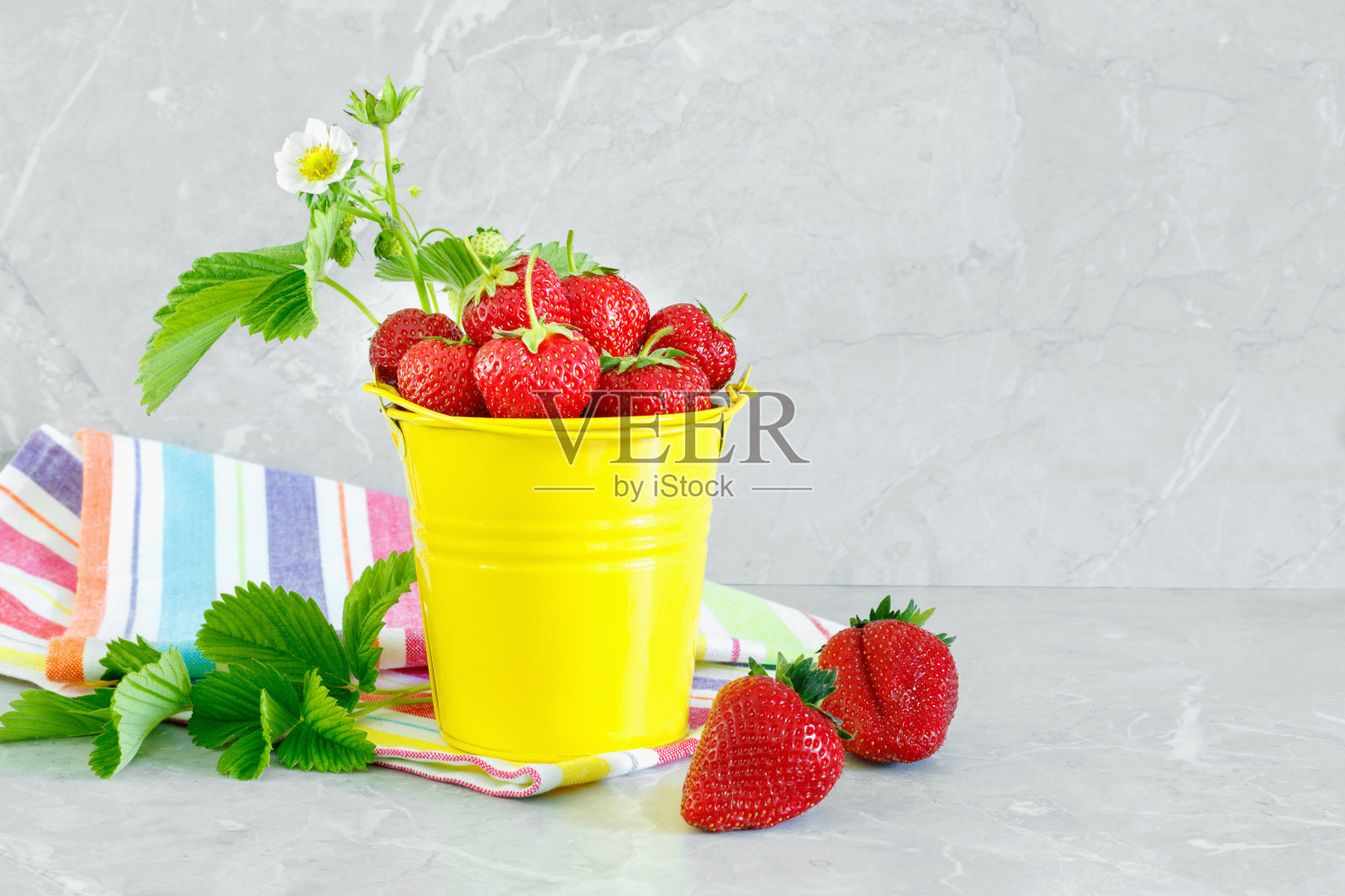 多汁的成熟美味的草莓在黄色的金属桶与条纹毛巾在石材台面。照片摄影图片