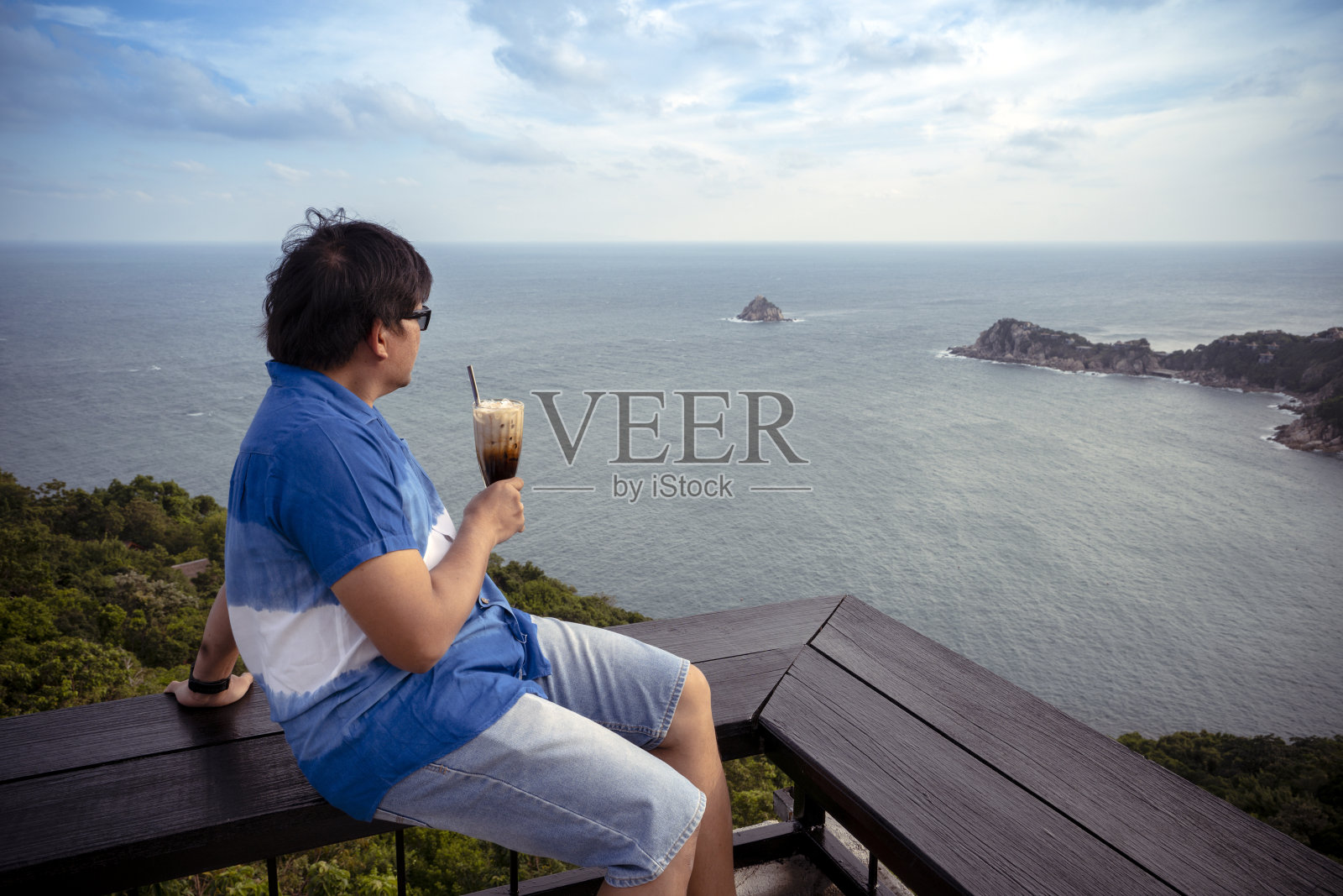 男人喝着咖啡，欣赏着海景照片摄影图片