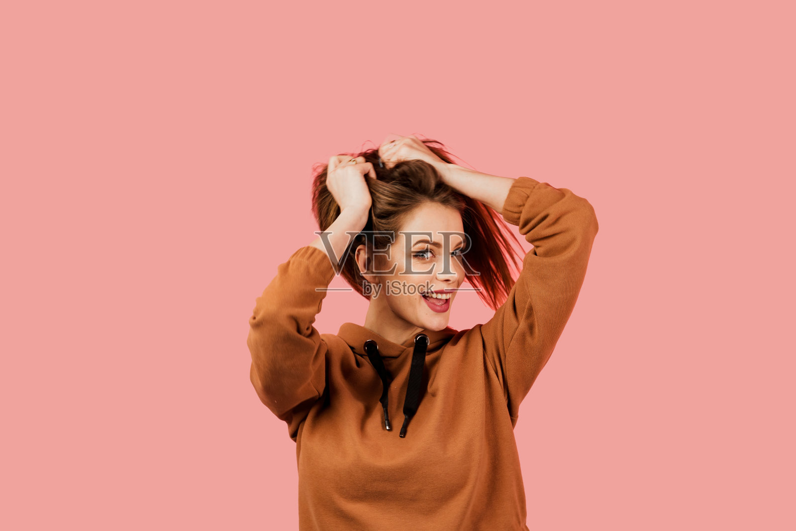 生活方式。鼓舞和快乐的女人微笑，大笑和苦笑在粉红色的背景。在摄影工作室摆姿势的模特。女孩穿着棕色的特大号服装照片摄影图片