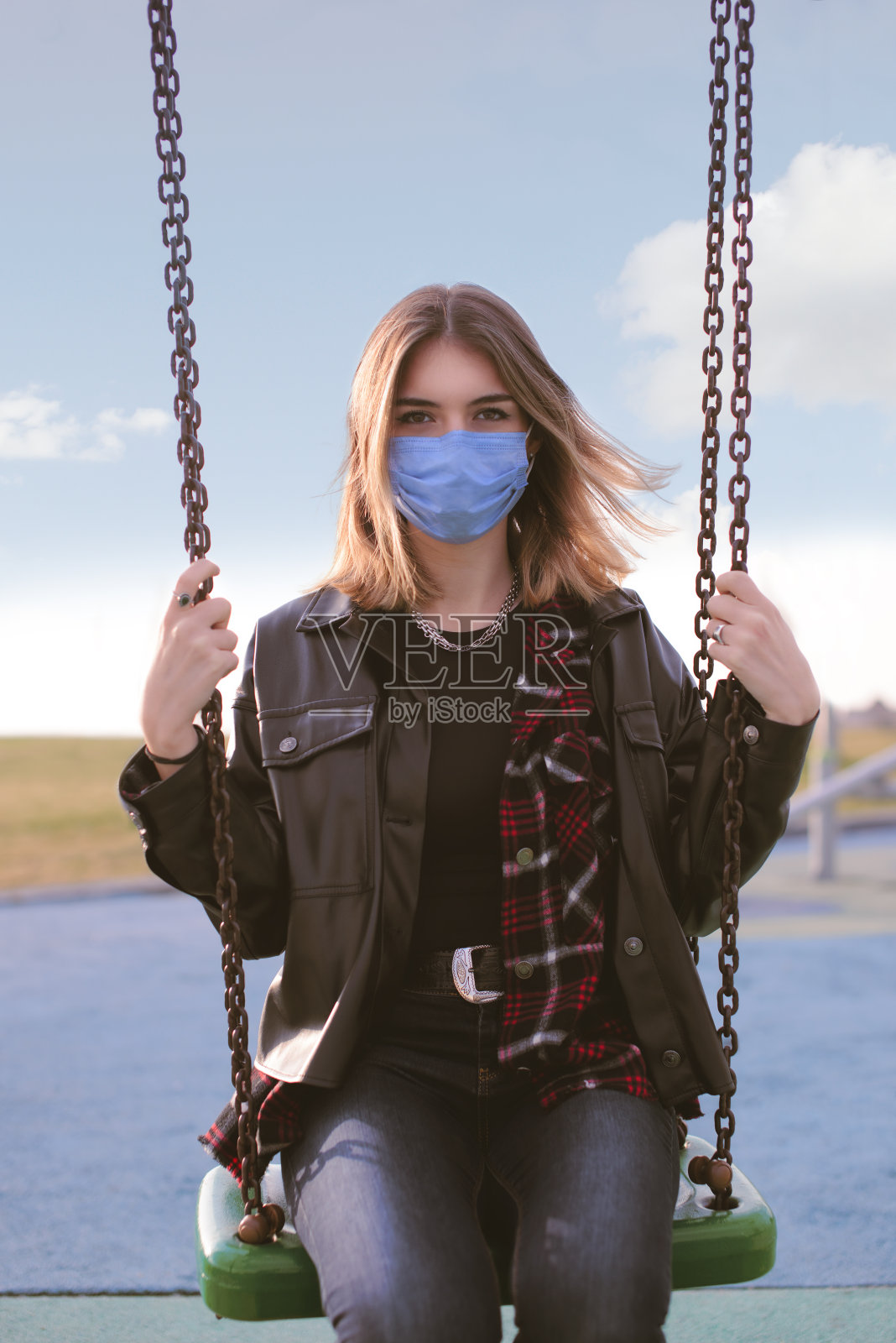 一个十几岁的女孩的肖像与医疗面罩在一个秋千和看着相机照片摄影图片