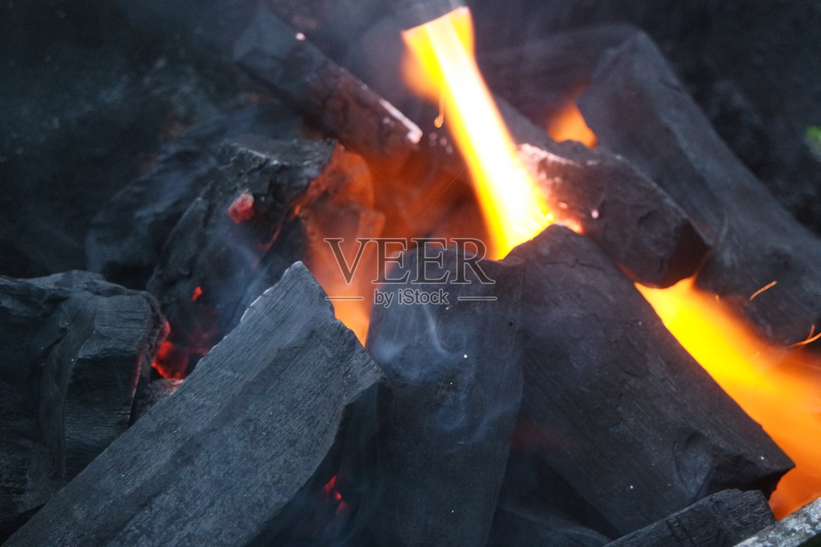 在有余烬和燃烧的煤和炽热的火焰的火锅中的原木。照片摄影图片