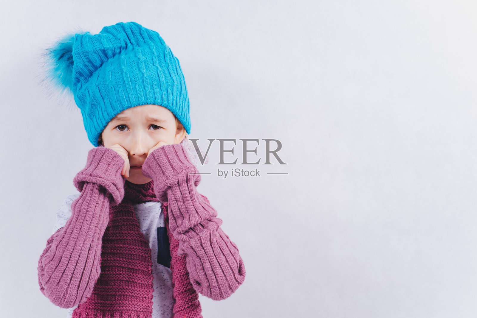 那孩子穿着冬衣站在白色的背景上。照片摄影图片