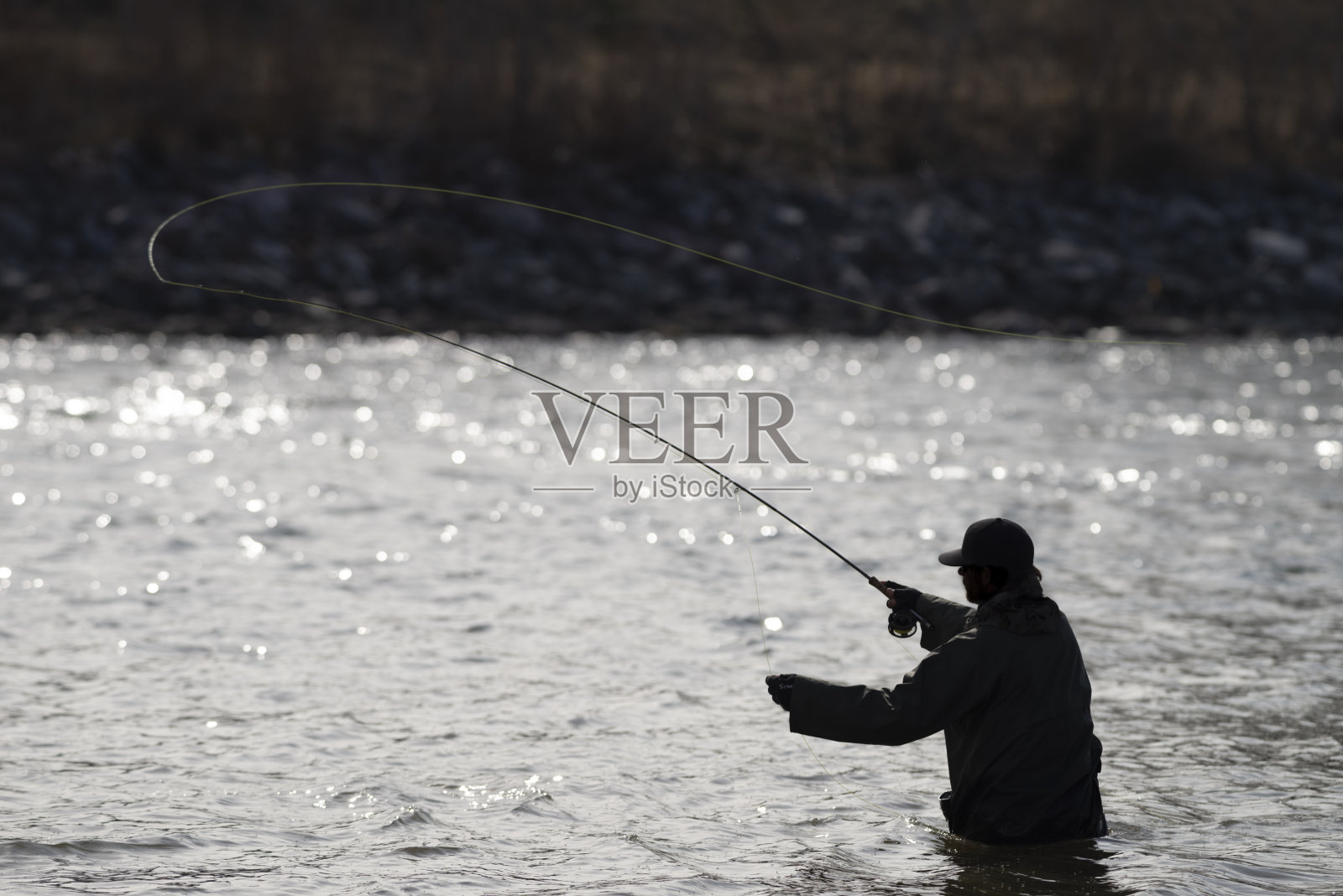 垂钓者在流动的河流中划出一条线，背光被太阳照亮照片摄影图片