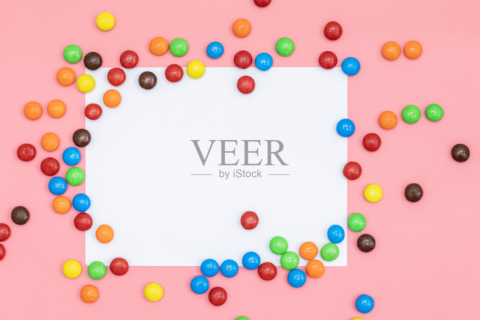 空白拷贝空间的文字白纸在中间，彩色巧克力涂层糖果在粉红色的背景与情人节。情人节概念节日食品礼物照片摄影图片