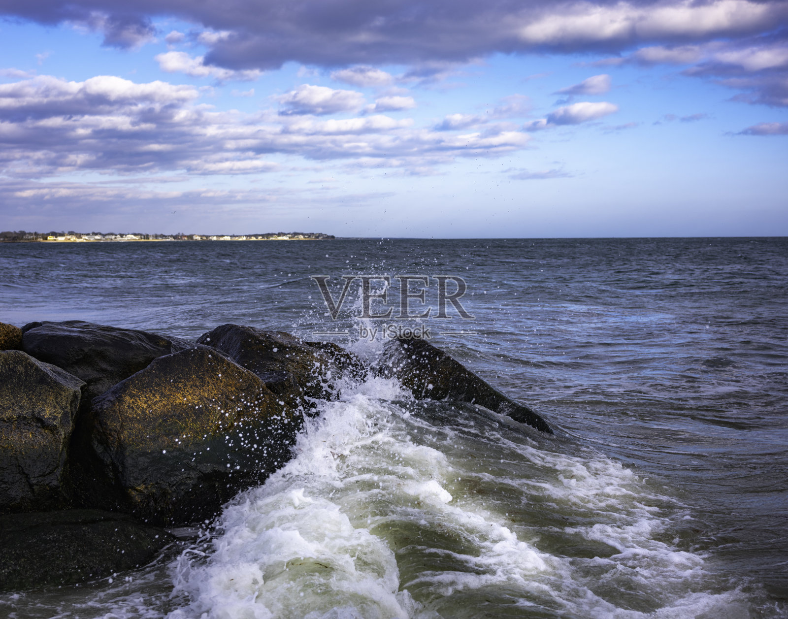 海景与溅起的潮汐波，暴风雨的云，和飞翔的海鸥在黑色的防波堤岩石照片摄影图片