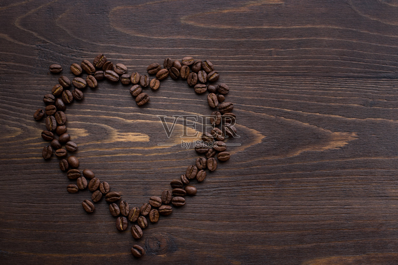 在棕色的木制背景上，烘烤的咖啡颗粒的形状和爱的象征的静物照片摄影图片
