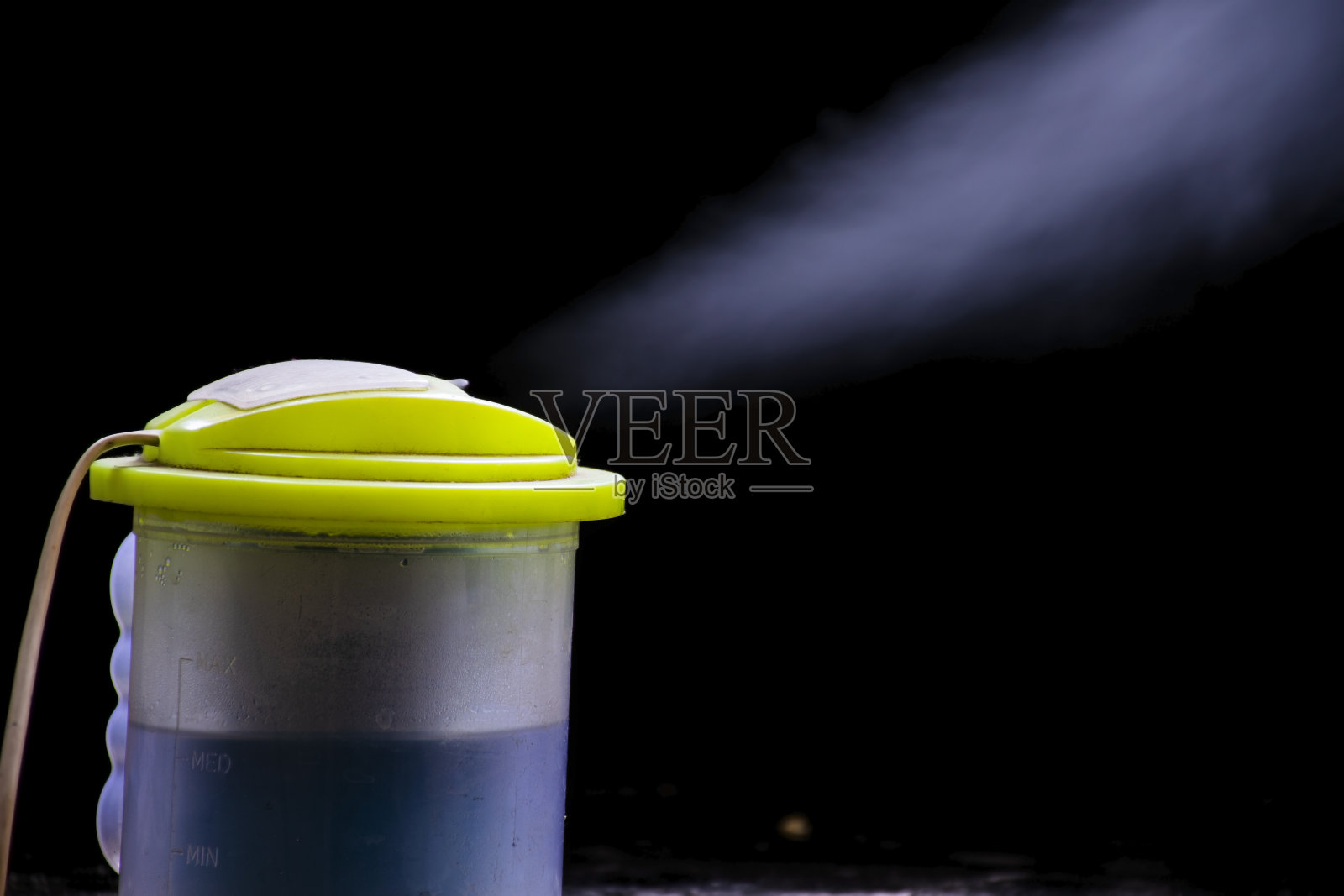 在漆黑的背景上，蒸汽从一个热水蒸笼的洞里冒出来。蒸笼是由塑料制成的。照片摄影图片