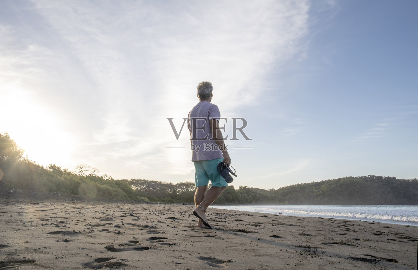 日出时分，一个人提着凉鞋走在沙滩上照片摄影图片