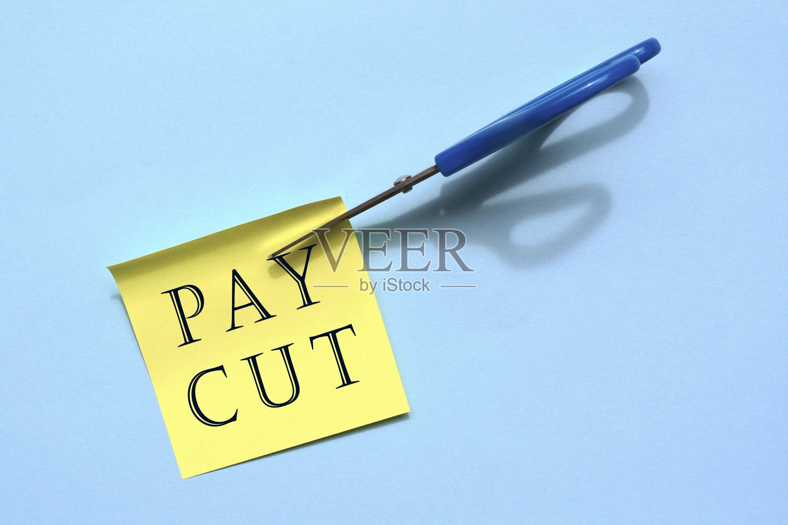 剪下蓝色背景上带有文字的黄色记事本的剪刀。经营理念，减薪照片摄影图片