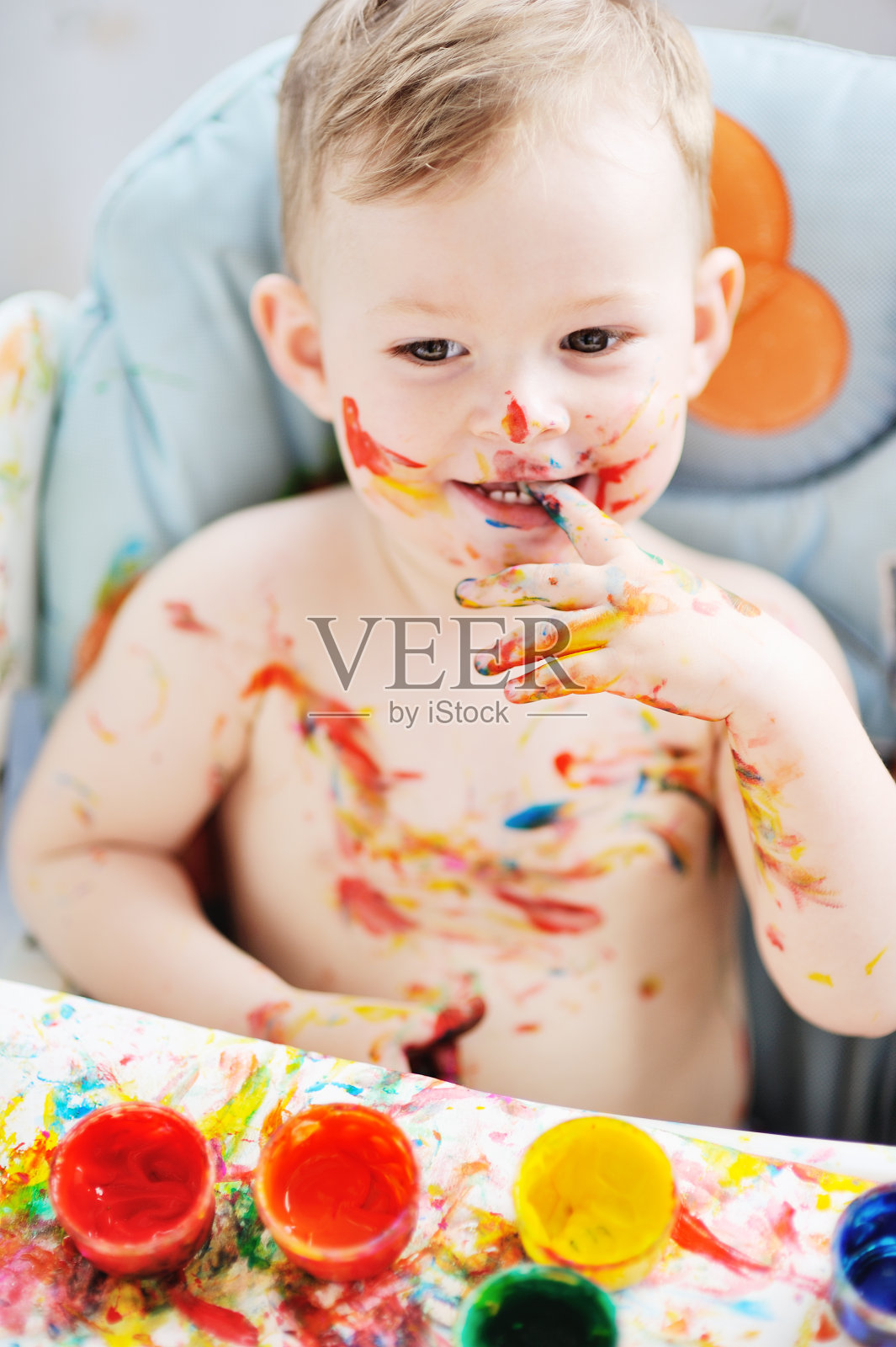 小男孩坐在桌子旁，把双手涂上了彩色颜料照片摄影图片